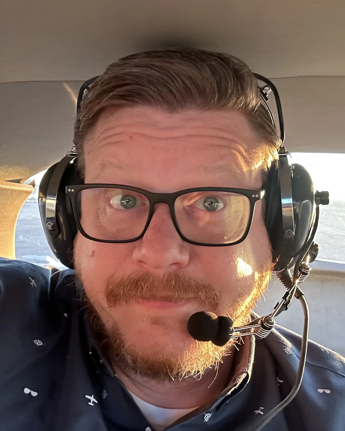 Greg Sullivan in the left seat of a Cessna, headset on, the sun low behind him